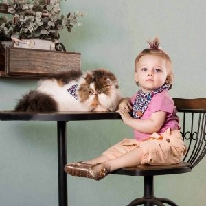 bebe junto com um gato sentada na cadeira usando  babador bandana estampa onça colorida