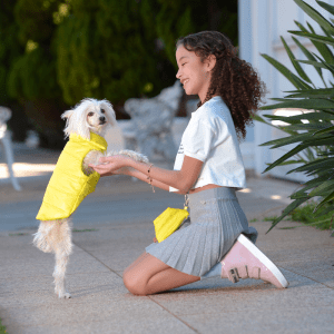 menina usando uma mini necessaire charlotte lima brincando com um cachorro usando um colete mood collors lima
